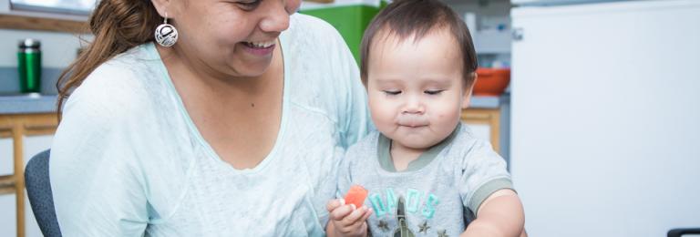 Mother with baby eating strawberries at a table.
